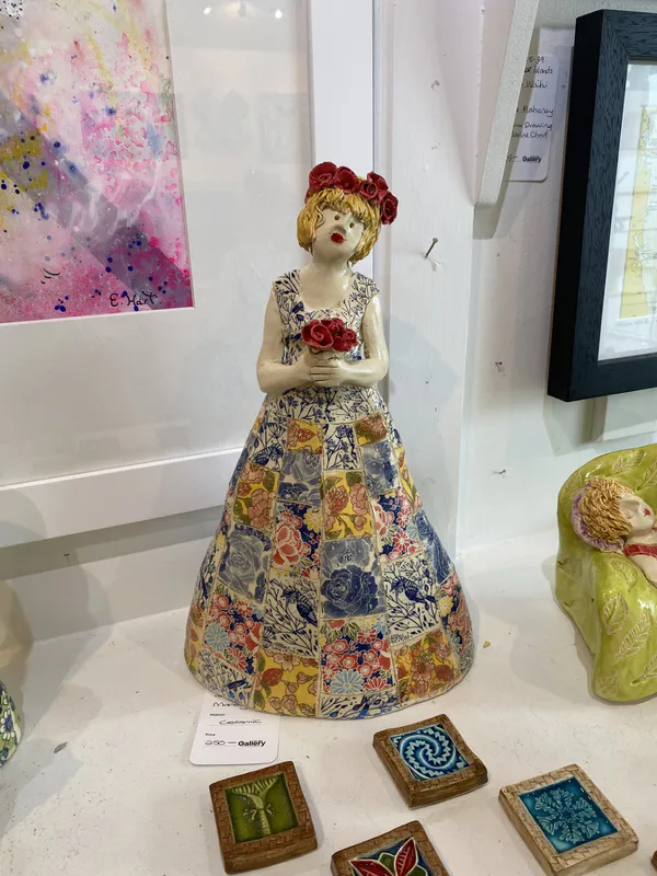 A handmade ceramic sculpture of a lady holding flowers wearing a patchwork dress by Mandy Olsen, available at The Little Gallery Tairua