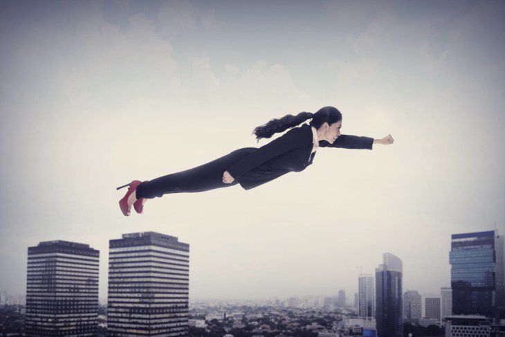 Woman in suit flying superhero-style over skyscrapers