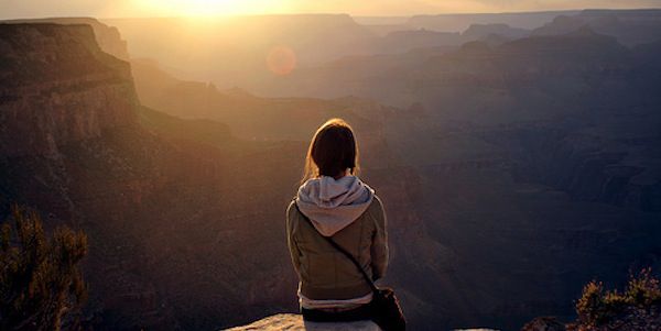 Photo of a woman sitting on a cliff-edge looking at the sunset